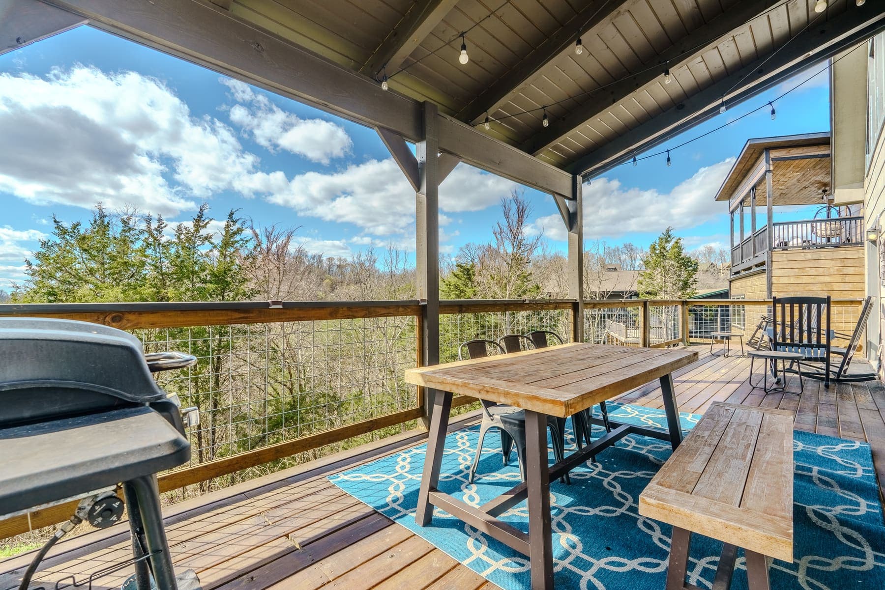 Covered deck dining — farmhouse table and bench under string lights