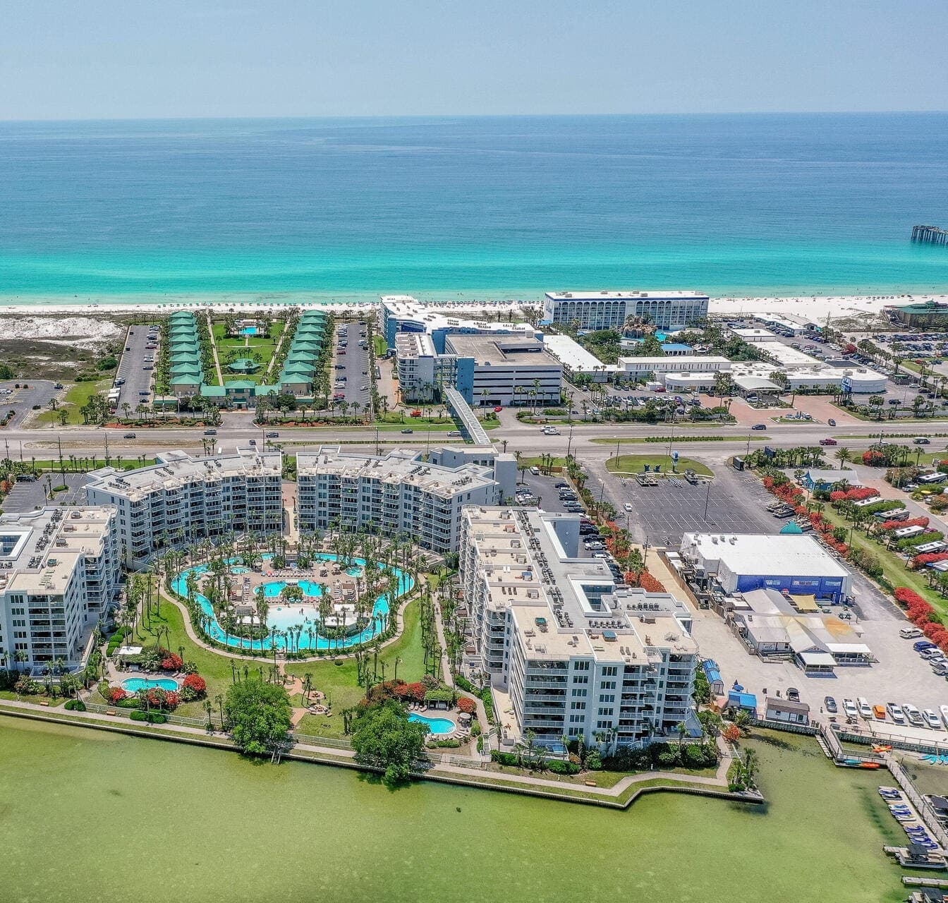Aerial of the Destin West resort — the lazy river winding between crescent condo towers, the emerald Gulf beyond