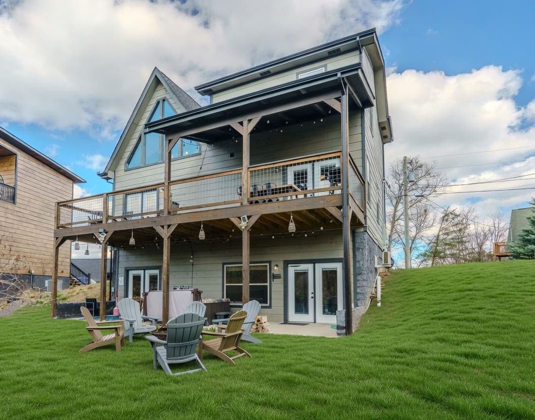 The lodge from the lawn: three stories, full-width double decks, Adirondack chairs circled around the fire pit