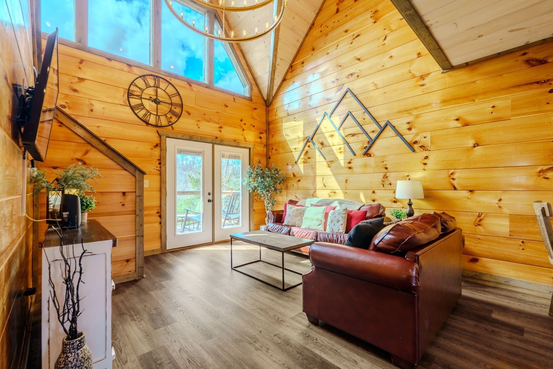 Vaulted great room with cathedral windows, gold ring chandelier, and mountain-range wall art