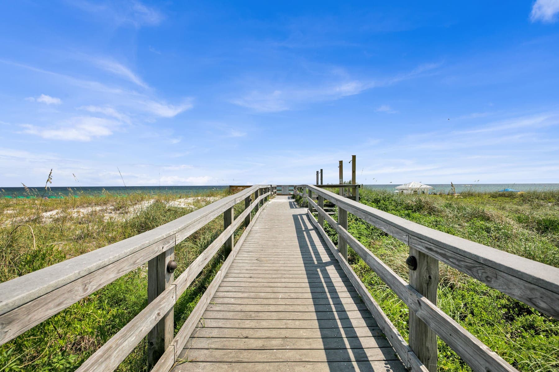Weathered boardwalk leading through dune grass toward the Gulf