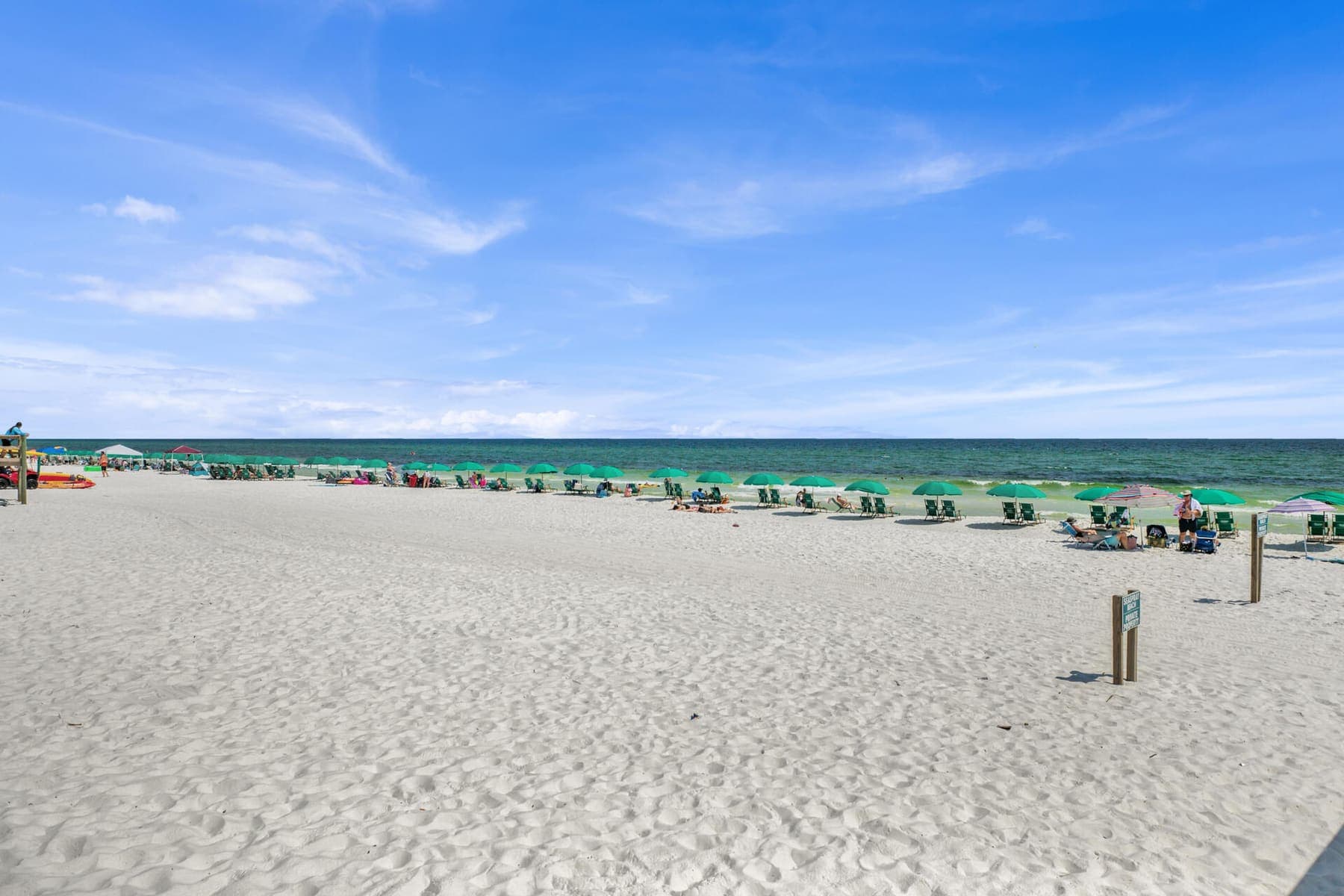 Sugar-white beach with a receding row of green umbrellas along emerald water